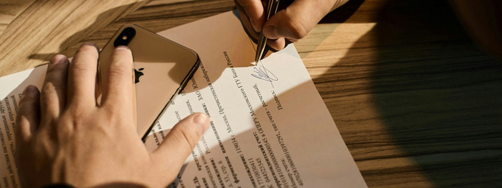 A hand signing a document on a wooden desk